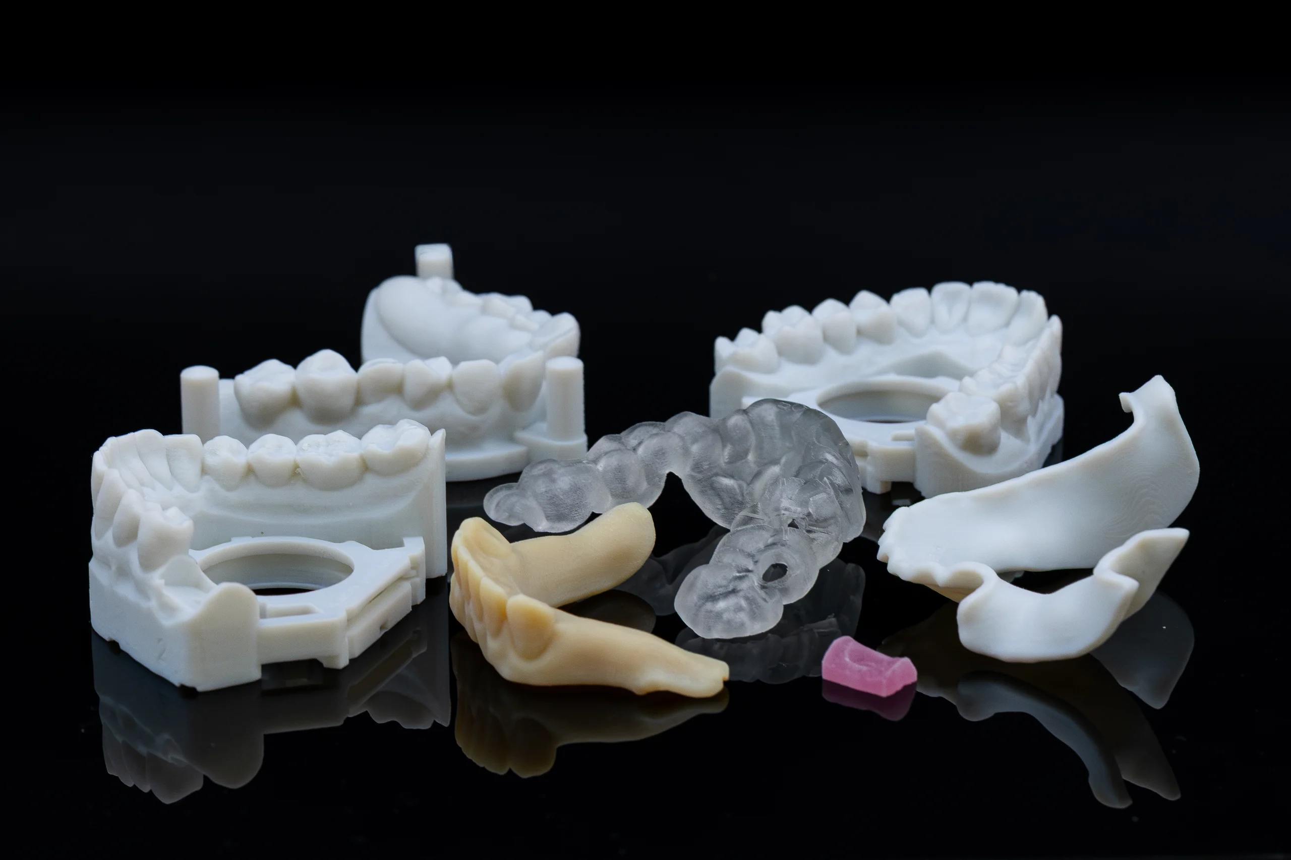 Unterschiedliche 3D-Druckergebnisse: Modelle, Schiene und weitere Druckteile auf dunkler Fläche